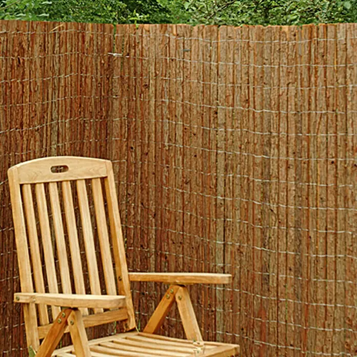 Gardol Comfort Rindholzmatte - 300 x 90 cm - Ein Holzstuhl steht vor einem blickdichten, natürlichen Weidenzaun, der Privatsphäre und ein rustikales Ambiente für den Garten bietet.