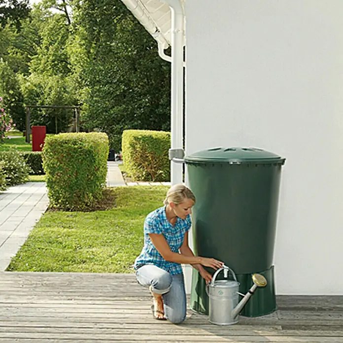 Regentonne - 300 l, Grün, Form: Rund - Frau befüllt eine Gießkanne aus einem Regenfass im Garten. Das grüne Regenfass ist ein praktisches Hilfsmittel zur Gartenbewässerung.