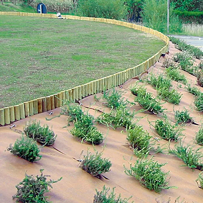 Gardol Premium Unkrautvlies Plus - Polypropylen, 10 x 1,15 m - Die ästhetisch ansprechende Landschaftsgestaltung umfasst einen Rasenbereich mit hölzerner Umrandung und einen bepflanzten Hang mit Bodengewebe.