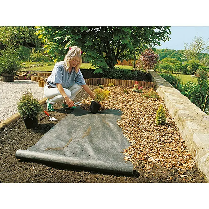 Gardol Premium Unkrautvlies - Polypropylen, 3 x 2 m - Gartenarbeit mit Unkrautvlies: Eine Frau pflanzt Setzlinge auf ein Beet, das mit einem schwarzen Unkrautvlies bedeckt ist.