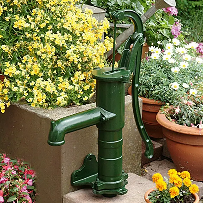 Floraworld Handschwengelpumpe Royal Classic - Winkelflansch, Max. Ansaughöhe: 7 m - Grüne Gartenpumpe aus Metall, umgeben von bunten Blumen. Ideal für die Dekoration und Bewässerung des Gartens.