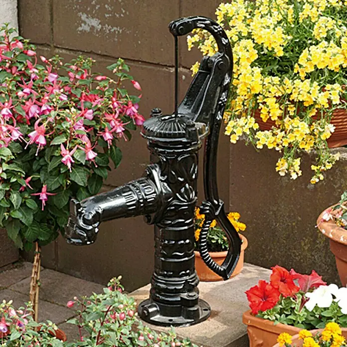 Floraworld Handschwengelpumpe Rustikal Classic - Max. Ansaughöhe: 7 m - Dekorative schwarze Wasserpumpe aus Gusseisen im Garten, umgeben von bunten Blumen.