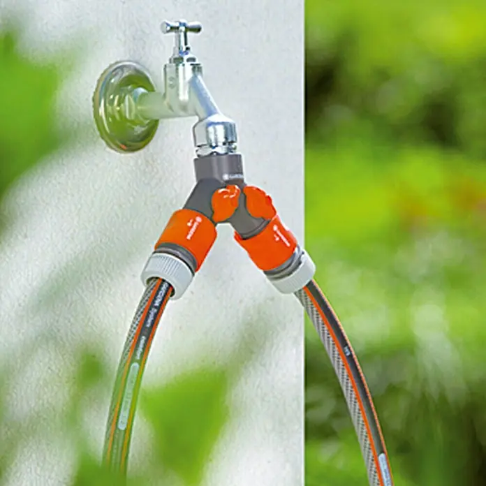Gardena 2-Wege-Ventil - Gewindegröße Wasserhahn: 33,3 mm (G 1″), Anschlüsse: 2 - Ein Wasserhahn mit einem Gardena-Doppelstück und zwei angeschlossenen Gartenschläuchen, ideal für die Gartenbewässerung.