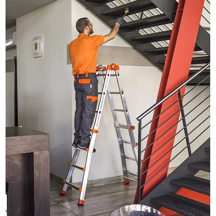 Gierre Mehrzweckleiter 4 + 4 - Anzahl Tritte: 16 Stk., Arbeitshöhe: 4,7 m, Belastbarkeit: 150 kg, Aluminium - Mann streicht von einer silber-orangen Mehrzweckleiter aus, die ihre Stabilität und Reichweite für Innenarbeiten demonstriert.