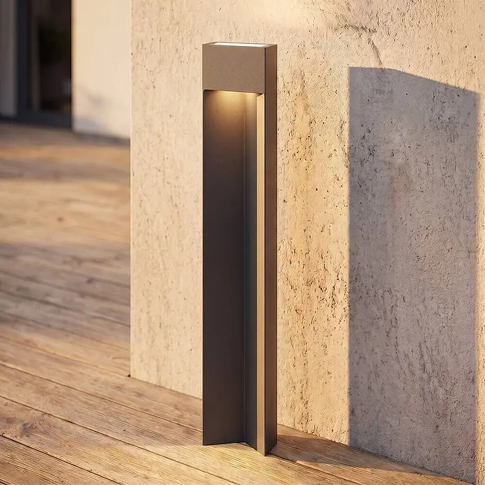 Lucande Außenlaterne Kaholo -  - Rechteckige anthrazitfarbene Außenleuchte beleuchtet eine strukturierte Wand und Holzterrasse.