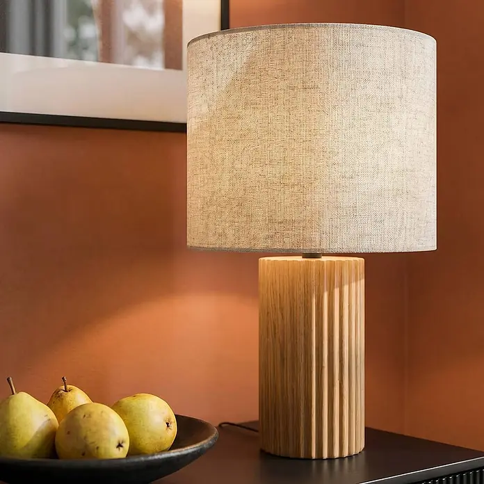 Lindby Tischleuchte Kimiko - Holz hell, E27 - Holztischlampe mit beigem Stoffschirm auf dunklem Tisch, neben Birnen.