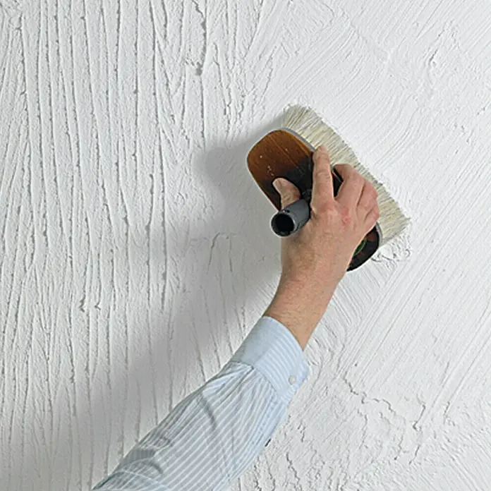 swingcolor Dekoputz Roll- & Streichputz - Weiß, Körnung: 1 mm, 20 kg, Konservierungsmittelfrei - Eine Person texturiert eine Wand mit einer Bürste. Die Textur ist vertikal und verleiht der Wand ein einzigartiges Aussehen.