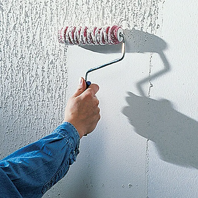 swingcolor Putzgrund - 5 l, Weiß - Eine Hand hält eine Strukturwalze, um eine Wand mit einer einzigartigen Textur zu versehen, die dem Raum Tiefe verleiht.