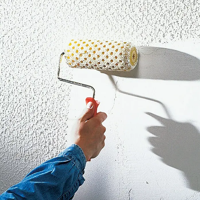 swingcolor Putzgrund - 5 l, Weiß - Nahaufnahme einer Hand, die eine Musterwalze an einer Wand benutzt, um eine einzigartige Textur zu erzeugen.