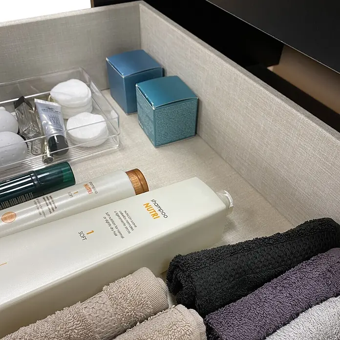Artysan Conjunto de mueble de baño Zion - Ancho: 80 cm, Teka y negro, 2 pzs. - Dos botellas blancas de champú 'NUTRI SOFT' organizadas en un cajón con toallas enrolladas y artículos de tocador.