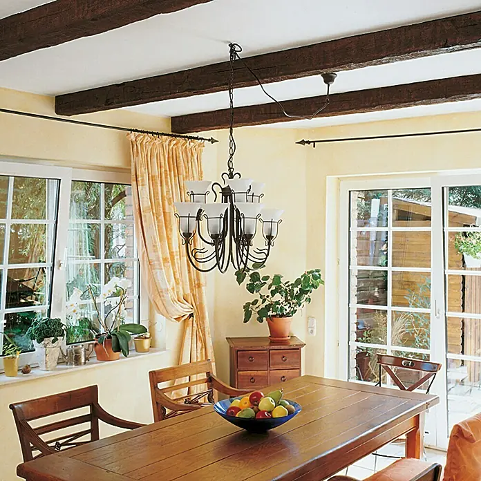 Decosa Viga decorativa Tirol - Roble oscuro, 2 m, Poliuretano - Una escena rústica de comedor con una elegante lámpara de araña, una mesa de madera y elementos naturales como plantas y frutas.