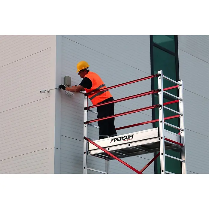 Andamio plegable Teletower - Altura de trabajo: 4,75 m, Ancho de la plataforma: 1,55 m, Longitud de la plataforma: 0,6 m - Andamio móvil plateado y rojo utilizado por un trabajador para instalar equipos en la fachada de un edificio.
