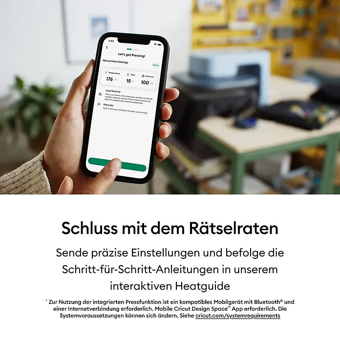 Cricut Transferpresse Autopress 2 - 53,5 x 41,3 x 29,4 cm, Drucktechnologie: Wärmeübertragung, Slate Blue - Eine Hand hält ein Smartphone, das eine App mit Einstellungen für die Hitzepresse und Anweisungen anzeigt. Eine Hitzepresse ist im Hintergrund zu sehen.