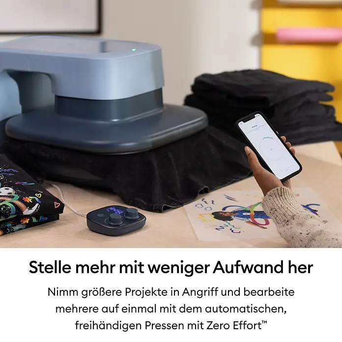 Cricut Transferpresse Autopress 2 - 53,5 x 41,3 x 29,4 cm, Drucktechnologie: Wärmeübertragung, Slate Blue - Eine große blaue automatische Heißpresse presst ein dunkles T-Shirt. Eine Person überwacht den Vorgang auf dem Smartphone; ein Steuergerät ist daneben.