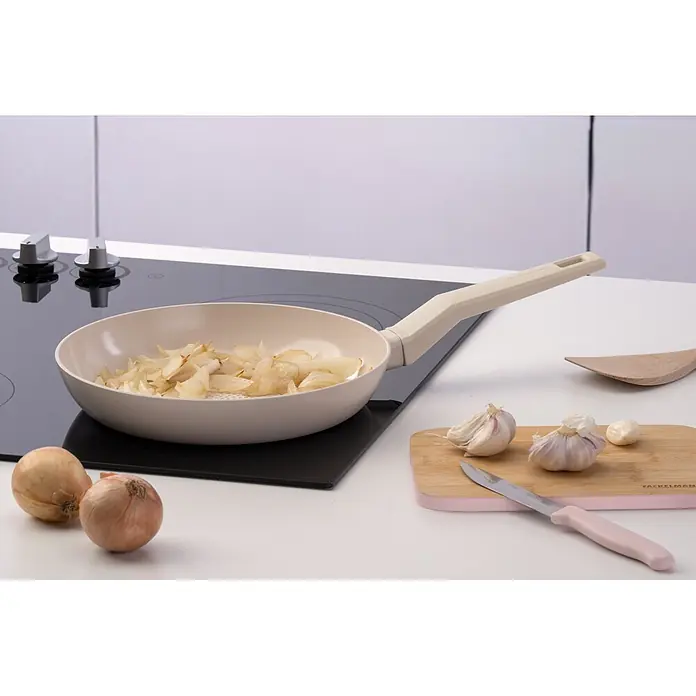 Fackelmann Pfanne Pamela Reif Kollektion Shell Wabenboden - Durchmesser: 24 cm, Beige - Beige Bratpfanne mit angeschwitzten Zwiebeln auf schwarzem Induktionskochfeld.
