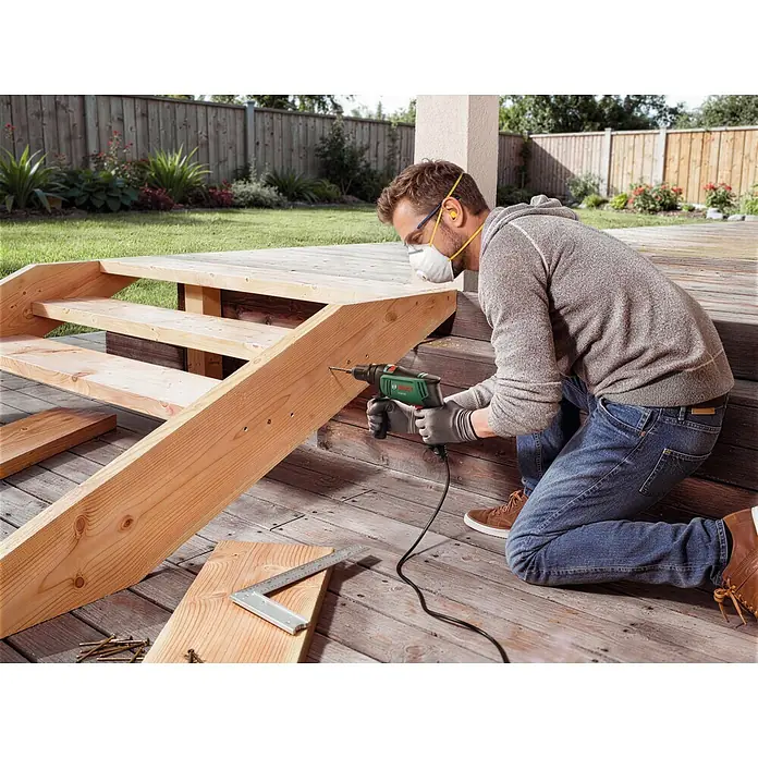Bosch Taladro percutor PSB750 - 550 W - 750 W, Portabrocas de sujeción rápida - Hombre taladrando madera para escaleras de terraza con un taladro Bosch verde y negro.