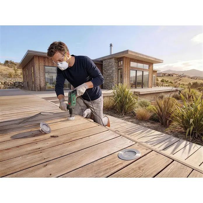 Bosch Taladro percutor PSB750 - 550 W - 750 W, Portabrocas de sujeción rápida - Hombre usa un taladro Bosch verde para cortar un agujero circular en una cubierta de madera para una luz empotrada plateada.
