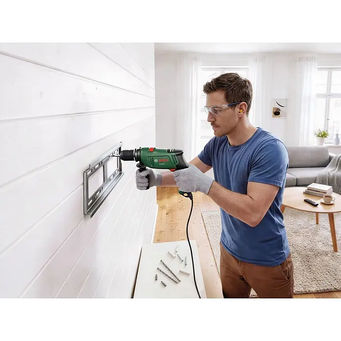 Bosch Taladro percutor PSB650 - 400 W - 650 W, Portabrocas de sujeción rápida - Hombre usa taladro Bosch verde y negro para instalar soporte de TV.