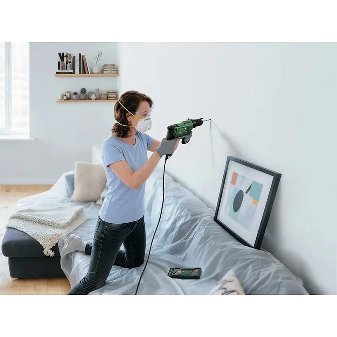 Bosch Taladro percutor PSB650 - 400 W - 650 W, Portabrocas de sujeción rápida - Mujer con equipo de protección taladra una pared con un taladro Bosch verde y negro.