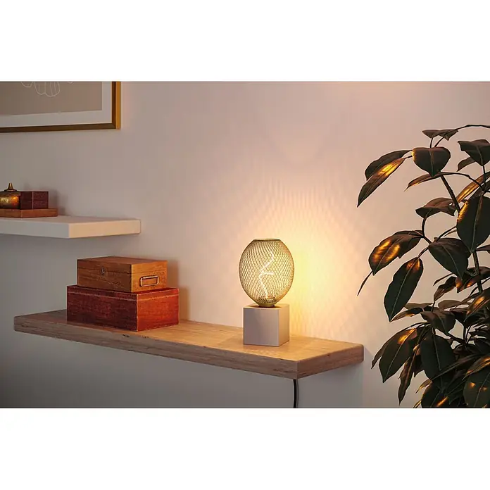 Paulmann LED-Lampe Globe Bernstein - E27, Warmweiß, 180 lm, 4 W - Eine goldfarbene Tischlampe mit Netzschirm und quadratischem Sockel beleuchtet ein Holzregal neben einer grünen Pflanze.