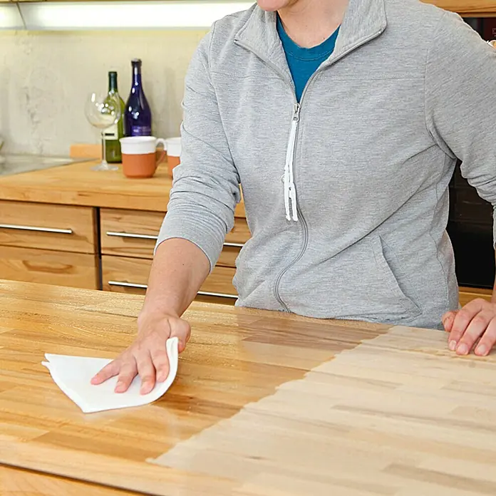 Osmo High Solid TopOilFarblos, 500 ml, Matt - Jemand trägt eine Holzlasur auf eine Küchentheke aus Holz auf, wobei die Hälfte bereits fertig ist und die Holzmaserung hervorhebt.