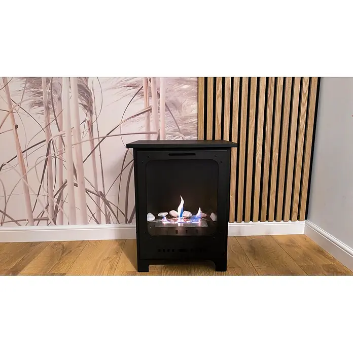 Bysil Kaminofen - Material Verkleidung: Stahl, Schwarz - Schwarzer Bioethanol-Kamin mit brennender Flamme und weißen Dekosteinen, auf einem Holzfußboden.