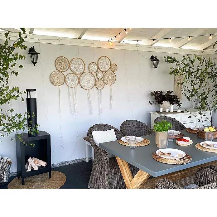 Bysil Kaminofen - Material Verkleidung: Stahl, Schwarz - Überdachte Terrasse mit grauem Esstisch, Korbstühlen und modernem schwarzem Kamin, schafft eine gemütliche Atmosphäre.
