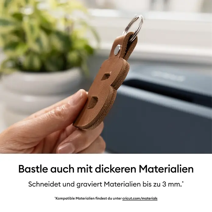 Cricut Maker Schneideplotter Maker 5 Essentials-Bundle - Schiefer, Bluetooth, Schnittbreite: 30,5 cm, Schnittlänge: 3,6 m - Hand hält einen braunen Leder-Schlüsselanhänger in Form des Buchstabens 'B' mit einem Metallring.