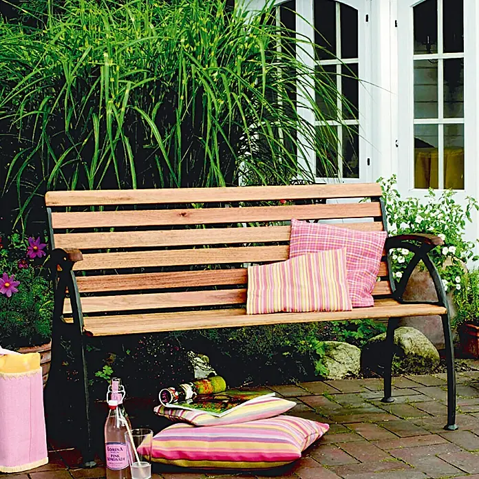 Bondex Teak-Öl - 2,5 l, Teak - Entspannen Sie auf dieser einladenden Gartenbank aus Holz mit bequemen Kissen vor einer üppigen Pflanzenkulisse.