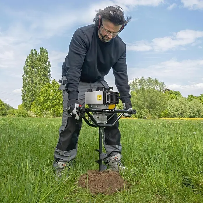 PowerPlus Ahoyadora POWXG50552 - 52 cm³, 1,4 kW, Anchura de trabajo: 10 cm - Hombre usa una ahoyadora POWERPLUS amarilla y gris con mangos negros para taladrar tierra.
