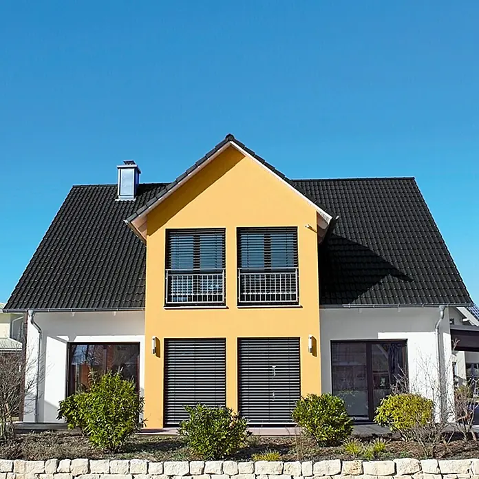 swingcolor Mix Dispersionsfassadenfarbe zum Mischen lassen - Basismischfarbe 1, 2,5 l - Modernes zweistöckiges Haus mit gelber Fassade, dunklem Dach und Fensterläden, umgeben von gepflegten Büschen und einer Steinmauer.