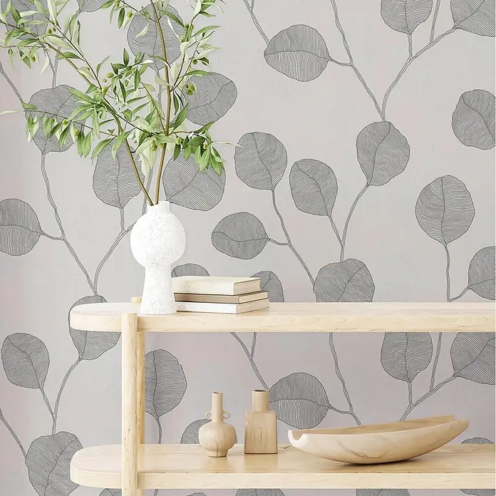 Marburg GZSZ Vinyltapete Blätterranke - Grau/Schwarz/Weiß, Floral, 10 x 0,53 m - Botanische Tapete mit grauem Blattmuster, hinter einem hellen Holzregal mit Deko und Pflanze.