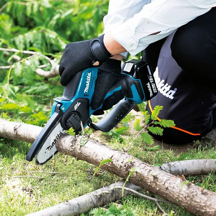 Makita LXT 18V Einhand-Akku-Kettensäge DUC101RX06 - 18 V, Li-Ionen, 2 Akkus, Schwertlänge: 10 cm - Person mit Handschuhen verwendet eine blaue und schwarze Makita Akku-Mini-Kettensäge zum Schneiden eines Astes.