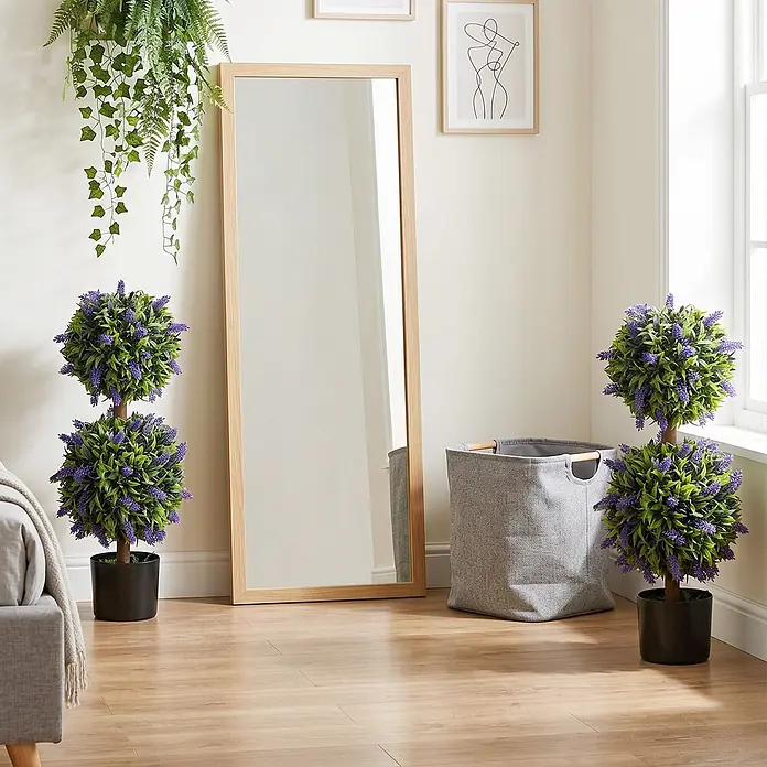Homcom Kunstpflanze Lebendiges Design -  - Ein hoher Spiegel mit Holzrahmen lehnt an der Wand, flankiert von zwei künstlichen Lavendel-Kugelbäumen in schwarzen Töpfen.