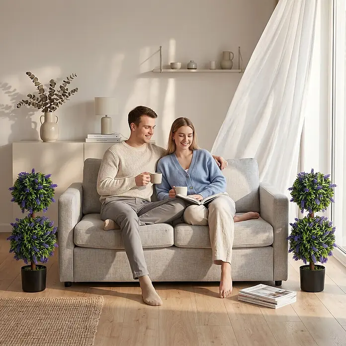 Homcom Kunstpflanze Lebendiges Design -  - Zwei künstliche Lavendel-Kugelbäume mit grünen Blättern und violetten Blüten in schwarzen Töpfen neben einem Sofa.