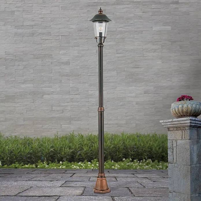 Orion Leuchten Außenlaterne Kenzo - 60 W, Farbe Gehäuse: Kupfer, 25 x 25 x 216 cm, Ohne Leuchtmittel - Hohe Außenlaterne in dunkler Bronzeoptik mit Klarglaslaterne, auf gepflasterter Terrasse stehend.