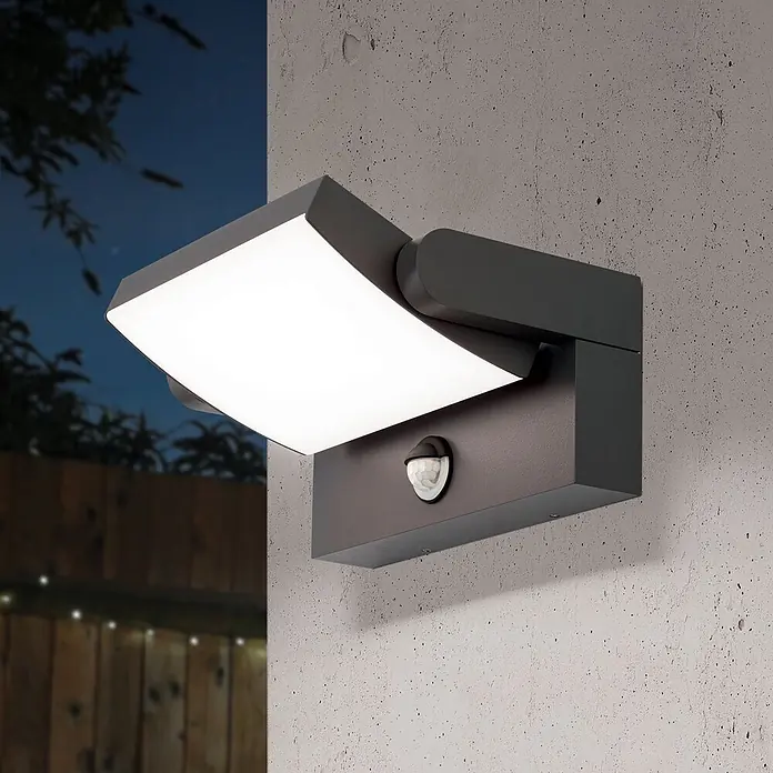 Orion Leuchten LED-Sensor-Außenwandleuchte Ginger - 21 W, L x B x H: 16 x 21 x 10 cm, Anthrazit, Opal, Warmweiß - Dunkelgraue Außenwandleuchte mit schwenkbarem Lichtpaneel und Bewegungsmelder, beleuchtet eine Betonwand im Freien bei Nacht.