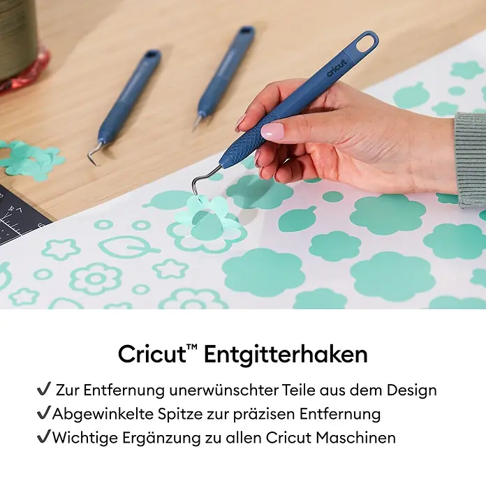 Cricut Plotter-Werkzeug Entgitterhaken - Geeignet für: Aufkleber, Blau - Eine Hand entfernt mit einem blauen Cricut Entgitterhaken überschüssiges Material von einem hellblauen Blumendesign auf einer Bastelmatte.