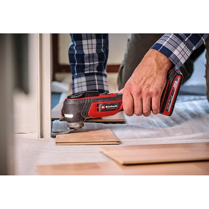 Einhell Professional PXC 18V Akku-Multifunktionswerkzeug E-Case TP-MG 18/3.6 LI BL - 18 V, Anzahl Akkus: Ohne Akku, Oszillationswinkel: -1,6 ° - 1,6 °, Sonstige - Kabelloses rot-schwarzes Einhell Multifunktionswerkzeug schneidet Holzfußboden an einem Türrahmen.