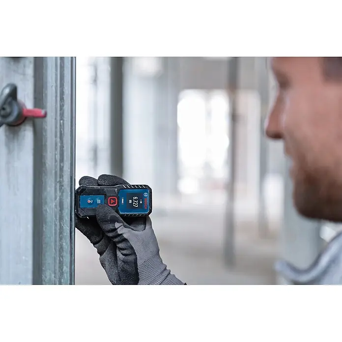 Bosch Professional Medidor de distancia láser GLM 50-21 - Gama de medición: 0,15 m - 50 m - Una persona con guantes de trabajo usa un medidor láser Bosch azul y negro para medir una viga metálica. Pantalla: 6.727 m.