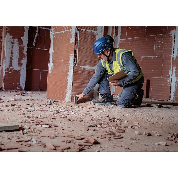Bosch Professional Medidor de distancia láser GLM 50-21 - Gama de medición: 0,15 m - 50 m - Trabajador de la construcción con equipo de seguridad utilizando un pequeño dispositivo de medición rectangular negro en el suelo de una obra.