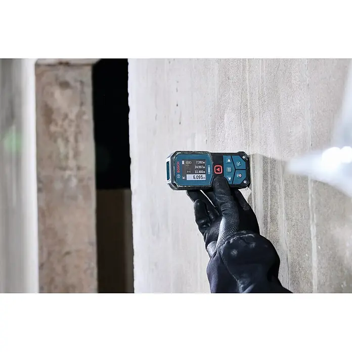 Bosch Professional Medidor de distancia láser GLM70-32 - Gama de medición: 0,05 m - 70 m - Medidor láser de distancia Bosch negro y azul, sostenido por una mano enguantada contra una pared, mostrando medidas en pantalla.