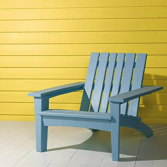 swingcolor Mix Buntlack Kunstharz für Außen zum Mischen lassen - Basismischfarbe 1, Hochglänzend, 750 ml, Lösemittelbasiert - Der blaue Adirondack-Stuhl vor einer gelben Wand ist einladend. Genießen Sie entspannte Stunden in diesem bequemen und stilvollen Gartenmöbelstück.