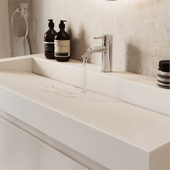 LOMAZOO Badmöbel-Set AZU-GW-WW-100 - Gesamtbreite Badmöbel: 100 cm - Nahaufnahme eines modernen weißen Badezimmerwaschbeckens mit einem silbernen Wasserhahn, aus dem Wasser läuft, und zwei dunklen Pumpflaschen am Rand.