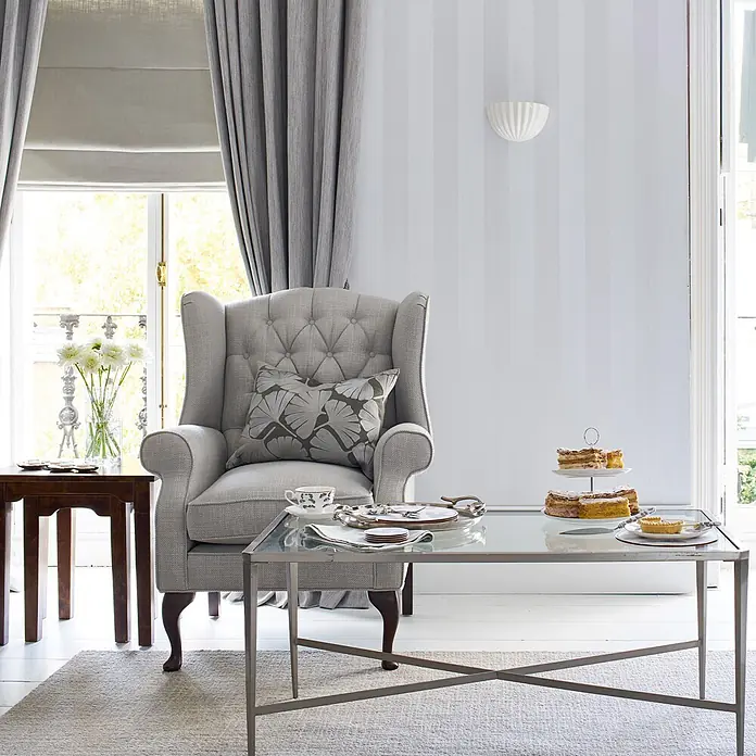 Lille -  - Ein gemütliches Wohnzimmer mit grauem Sessel, gläsernem Couchtisch mit Kuchen und Holztisch am Fenster.