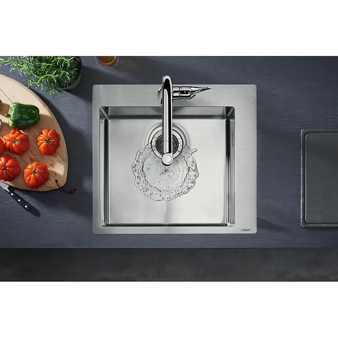Hansgrohe Einbauspüle S711 - 50,5 x 50 cm, Edelstahl - Verchromte Küchenarmatur spendet Wasser in ein gebürstetes Edelstahlspülbecken, daneben frisches Gemüse auf einem Schneidebrett.
