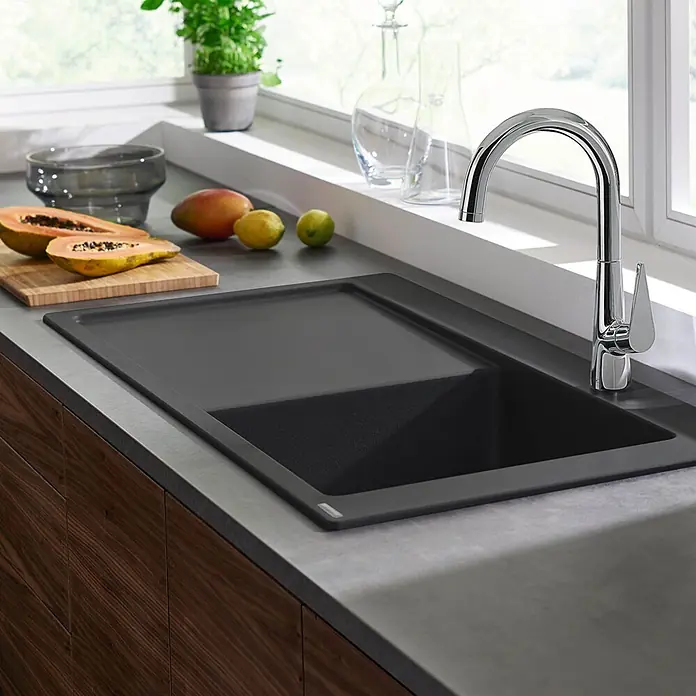 Hansgrohe Einbauspüle S51 - 105 x 51 cm, Graphiteschwarz, Position Ablage: Links - Dunkelgraue Küchenspüle mit integriertem Abtropfbereich und Chromarmatur in moderner Küche mit Obst.