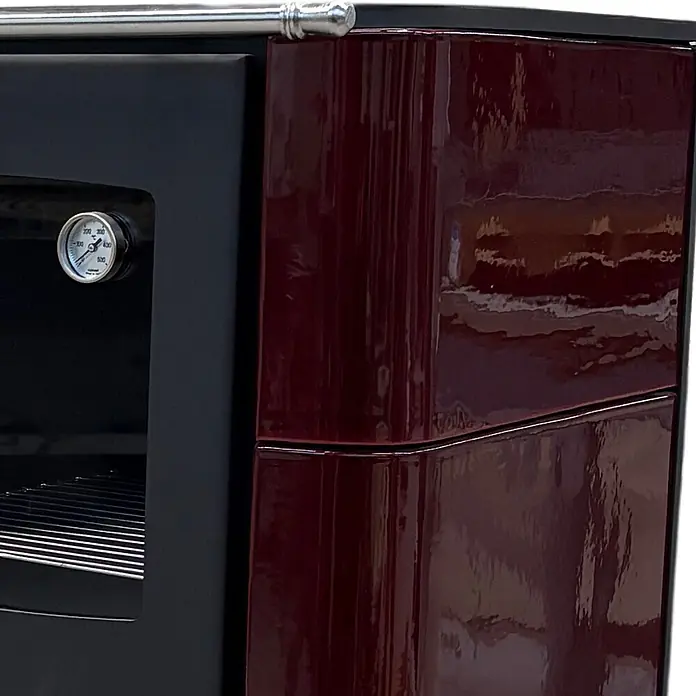 Domofire Kaminofen Sparherd Steyr M - 7,5 kW, Raumheizvermögen: 150 m³, Material Verkleidung: Keramik, Schwarz - Ofenabschnitt mit schwarzer Tür, internem Thermometer und glänzender dunkelroter Seitenverkleidung mit silbernem Griff.