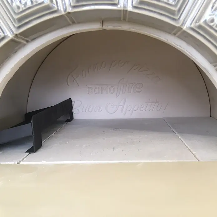 Domofire Kaminofen Capri - Material Verkleidung: Keramik, Weiß - Heller Pizzaofen-Innenraum mit gewölbter Öffnung und geprägtem italienischem Text 'Forno per pizza DOMOfire Buon Appetito!'.