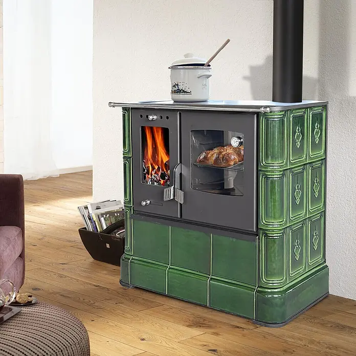 Domofire Kaminofen Sparherd Steyr - 7,5 kW, Raumheizvermögen: 150 m³, Material Verkleidung: Keramik, Schwarz - Grüner Kachelofen mit Ofenfenster, Brot backend, Feuer brennend und Topf obenauf, in einem Wohnzimmer.